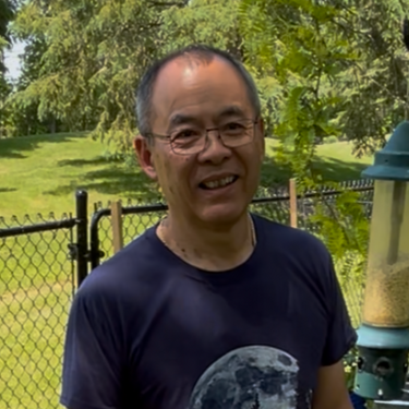 Man standing in a grassy area with trees and in the background. Ellery reviewing the lila composter