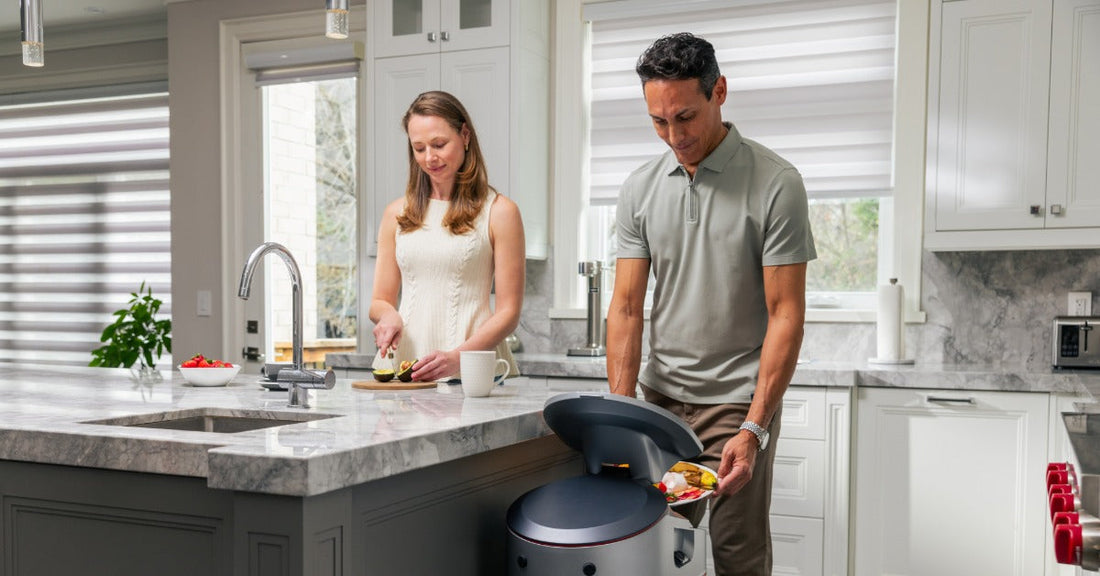 A woman slicing avocado while a man discards food scraps into a kitchen bin beside a marble countertop.