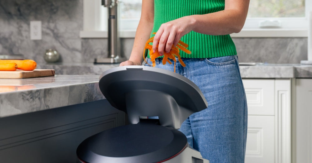 Hand throwing carrot peels into LILA electric kitchen composter