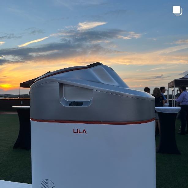 LILA Pro smart kitchen composter displayed at an outdoor sustainability event during sunset.